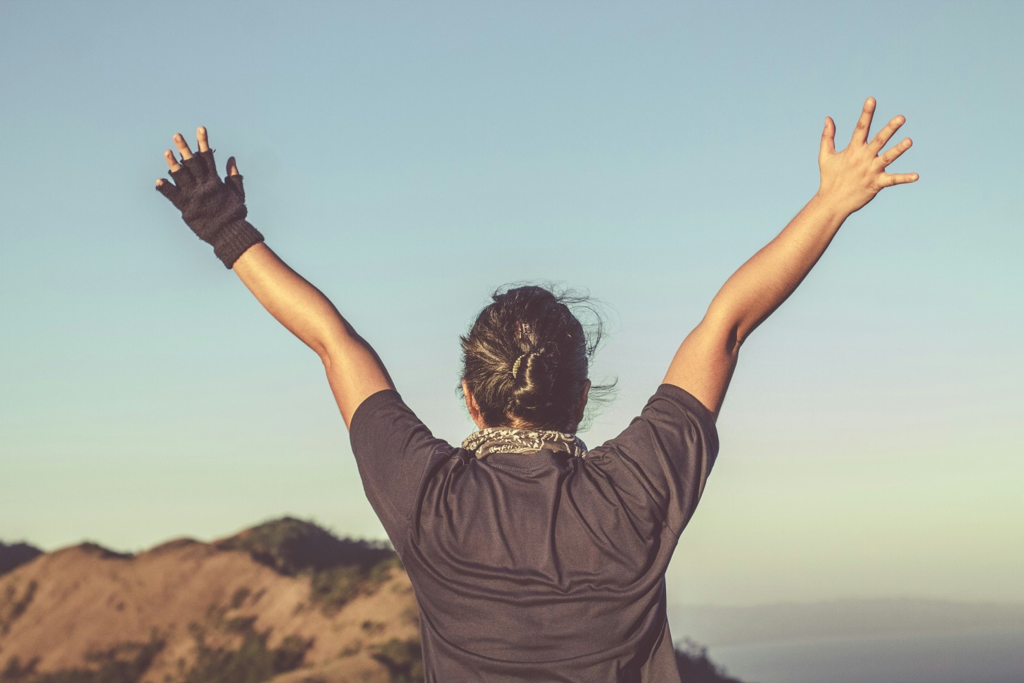 person holding arms up at the top of a mountain